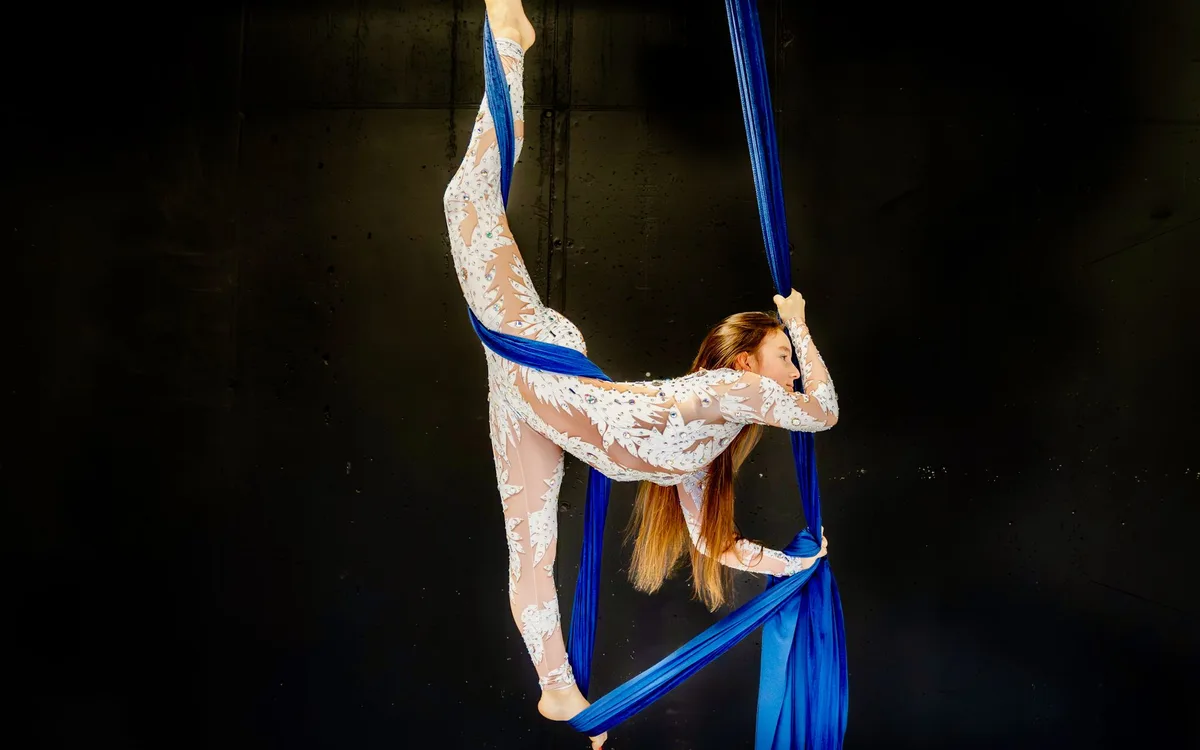 An aerialist suspended above the stage on silks during a water-stage production
